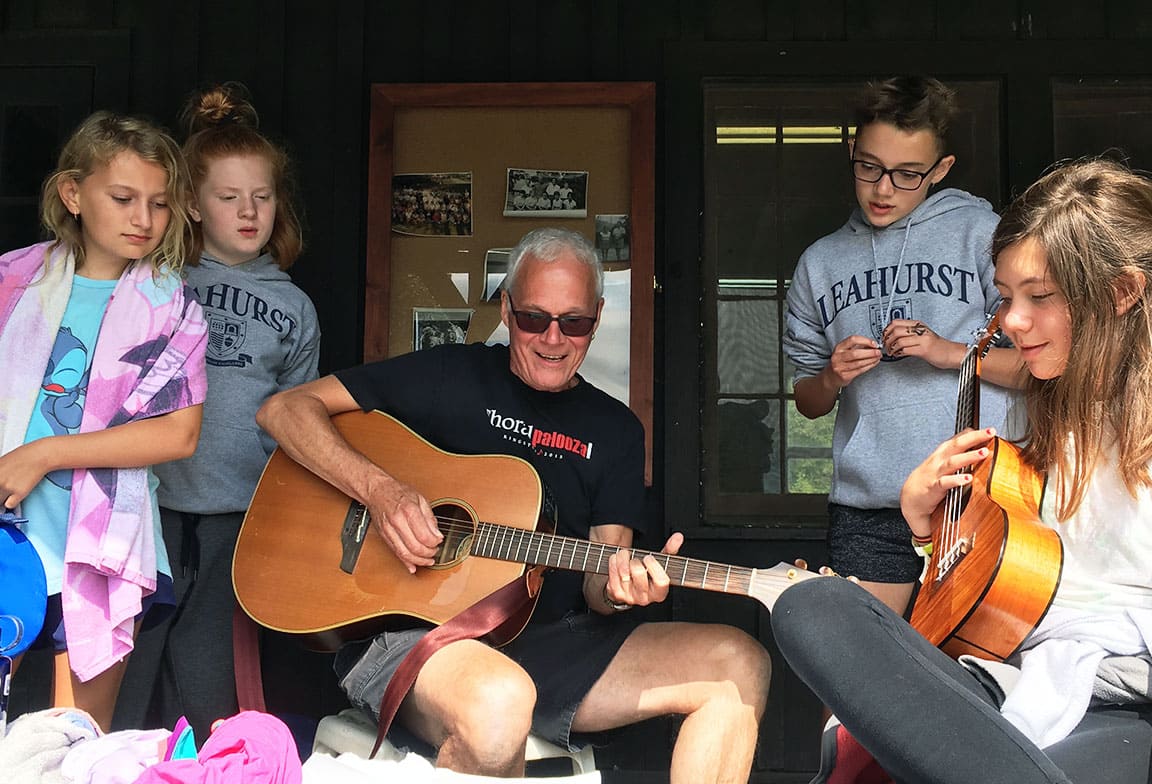 Picture of a teacher playing the guitar with students at a camping outdoor education activity